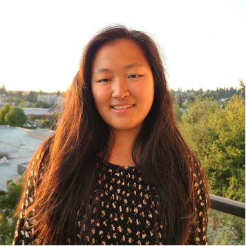 A smiling woman with long brown hair wearing a black shirt with white polka dots.