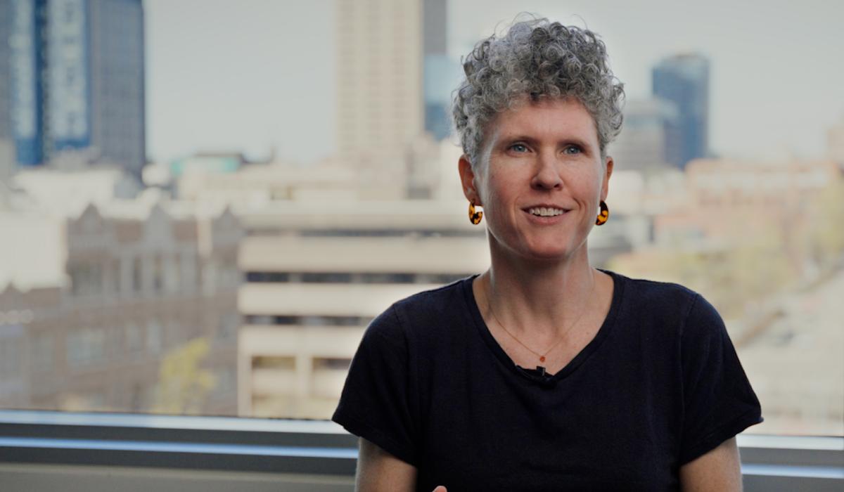 Joan Casey smiles in front of a window with blurry buildings in the background.