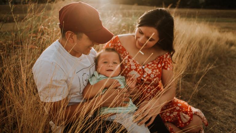 A man and woman hold a smiling child in a field of tall grasses.