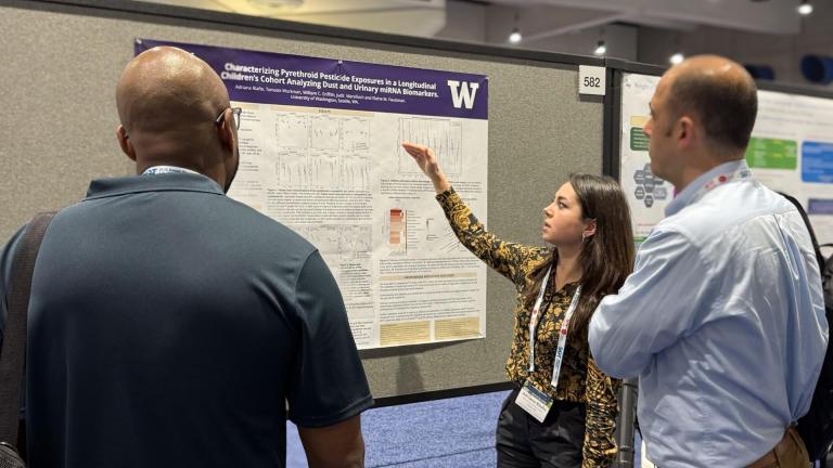 Adriana Riaño points to her research poster while two people look on.