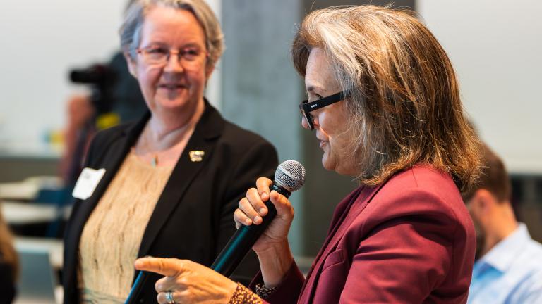 Tracey Woodruff speaks into a microphone while Lianne Sheppard looks on.