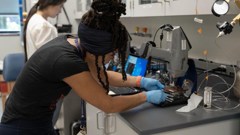 Dawn Johnston leans over a work bench in a scientific lab to touch a microscope slide.