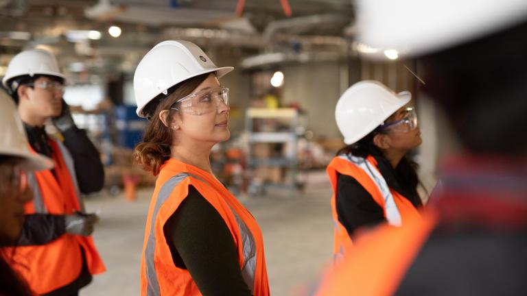 Dennise Drury stands in a hard hat and safety vest in an industrial space with other students around her.