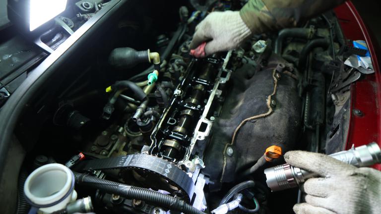 Hands inside of a car's hood, working on the engine.