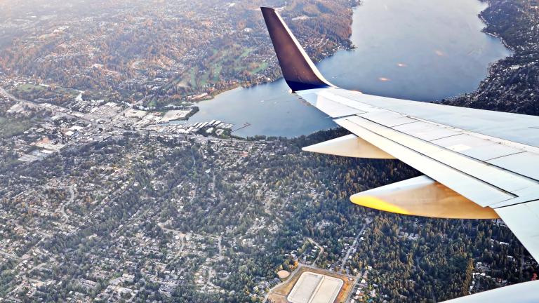 Aerial view shows wing of an airplane flying over a residential neighborhood