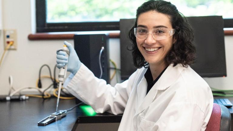Erica Fuhrmeister smiles holding a micropipet in a lab.