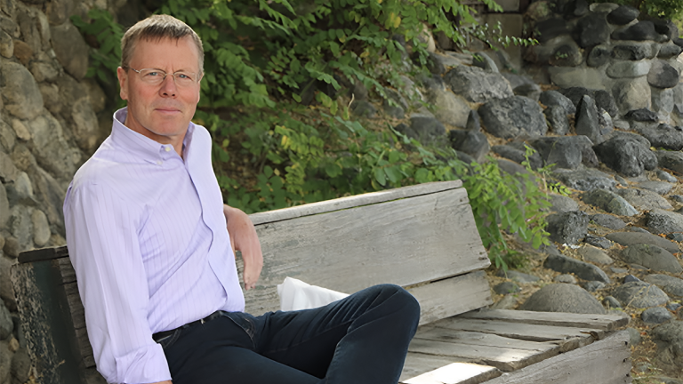 Steven Gilbert sits on a bench outside smiling.