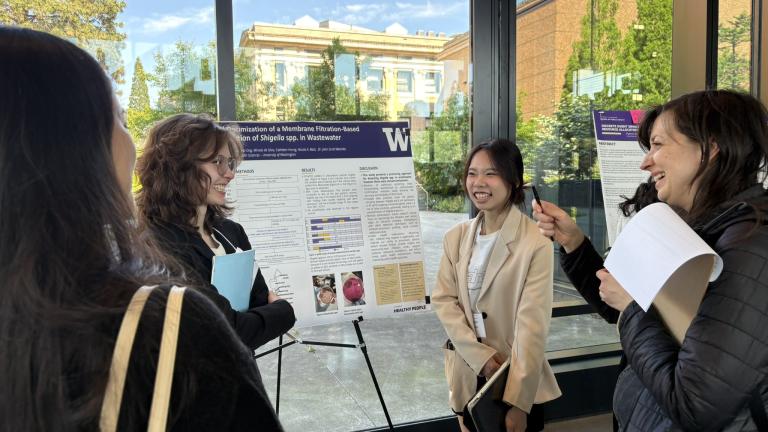 Four people stand around a research poster smiling and interacting.