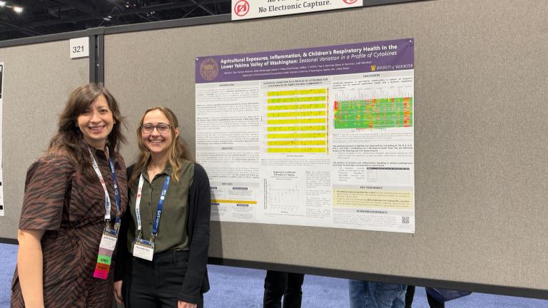 Judit Marsillach and Hannah Dye stand together in front of a research poster.