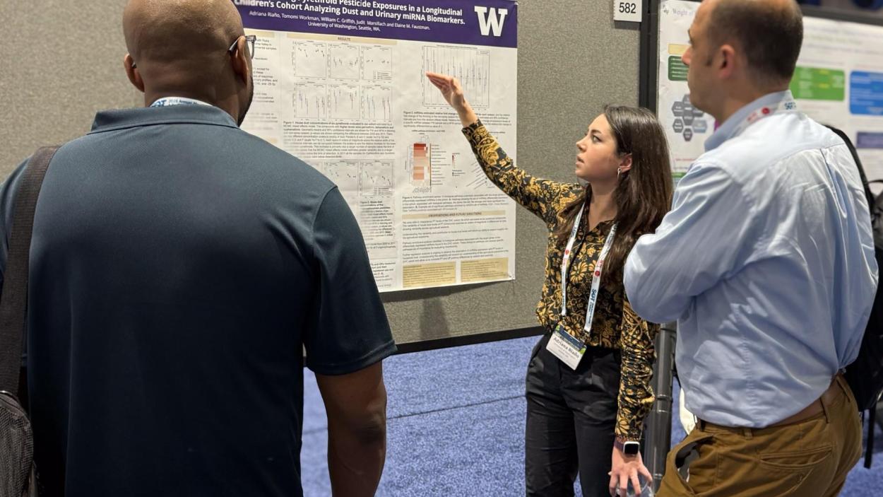 Adriana Riaño points to her research poster while two people look on.