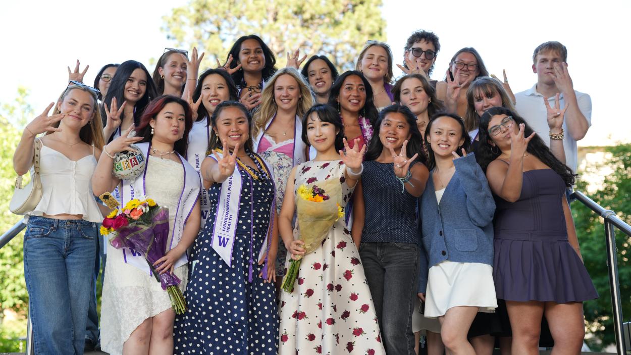 A large group of undergraduates stand together outside holding up "W" symbols with their fingers in honor of the University of Washington. 