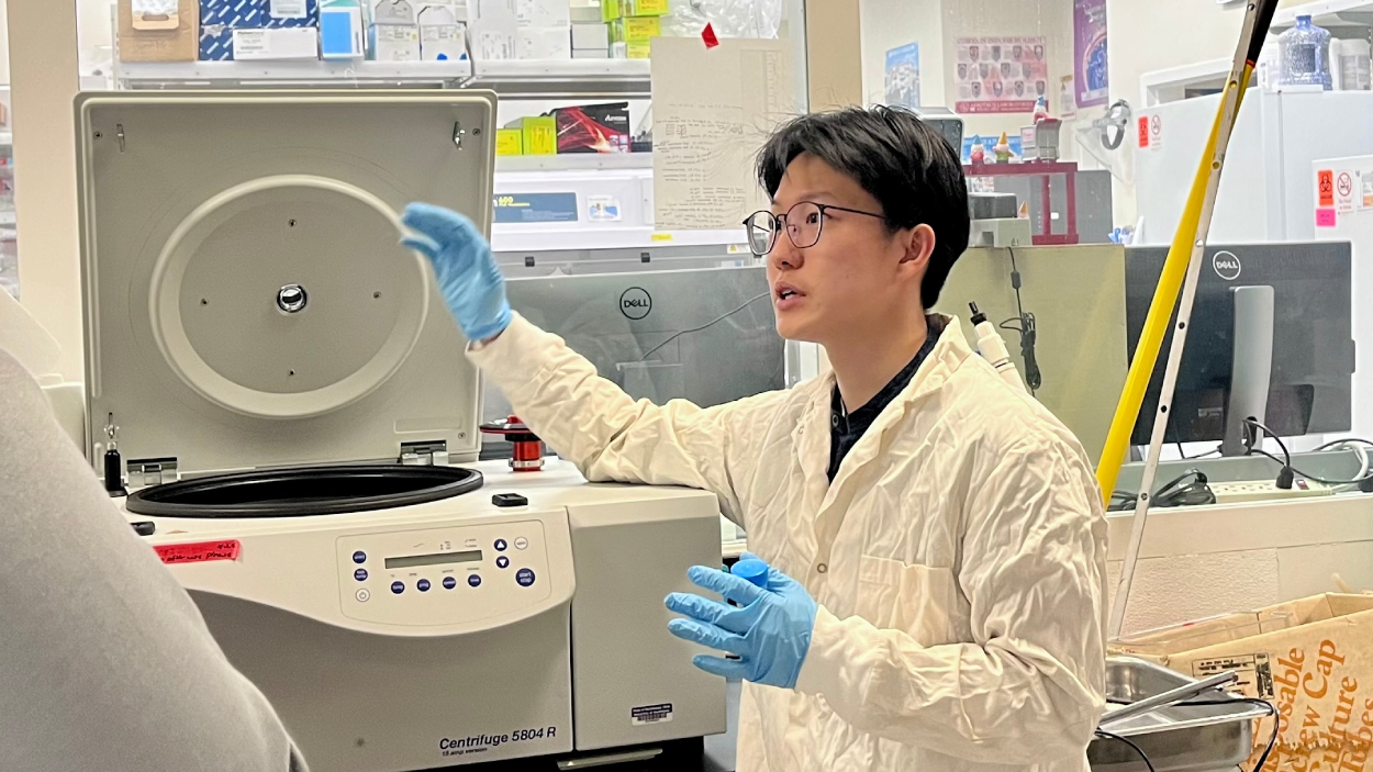 Angelo Ong gestures toward a centrifuge in a lab.