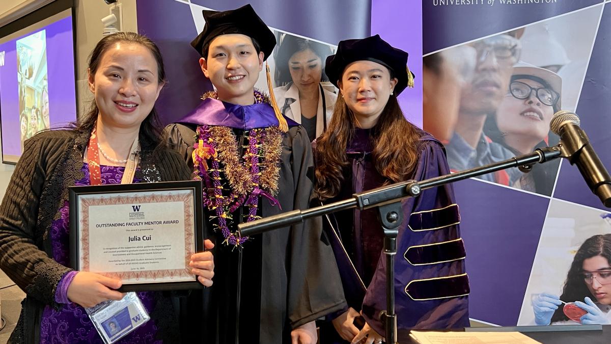 Julia Cui stands holding a framed award reading "Outstanding Faculty Mentor Award" next to Joe Lim and Sarah Kim, both wearing graduation regalia. 