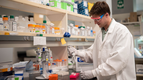Student in a white lab coat working in a lab.