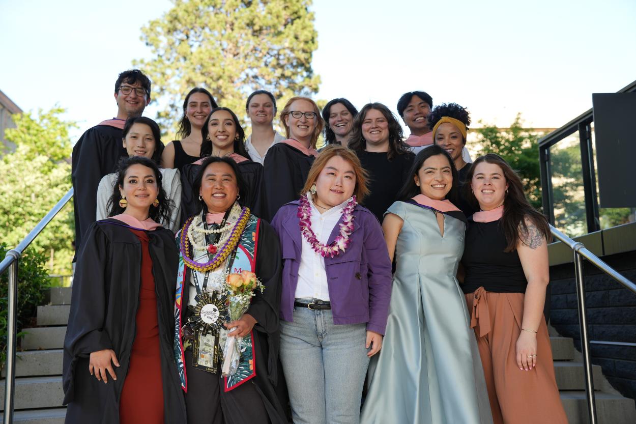 A large group of master's students stands outside together in a group to celebrate their graduation.