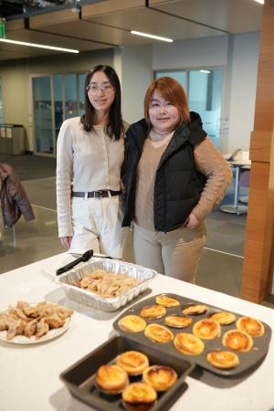 Hao and another student stand behind a counter with lots of foods for a Lunar New Year celebration.