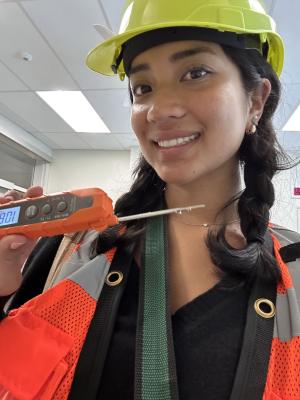 Emily Do, wearing a safety vest and hard hat, holds a temperature sensor in her hand.