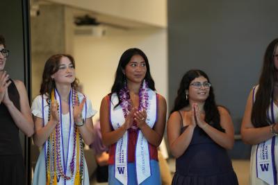 Angelina Durbin, Emily Do and another student stand clapping in graduation regalia.