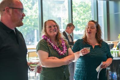 Amy Gundlach Ritter smiles wearing a lei as two other people look on.