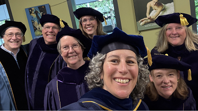 Seven professors in graduation regalia stand together smiling.