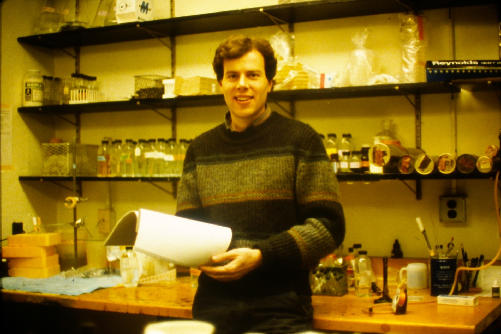 Cangelosi smiles holding an open notebook in a lab.