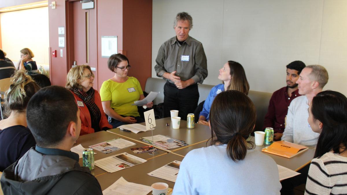 Tom Burbacher stands, presenting to a round table of seated people
