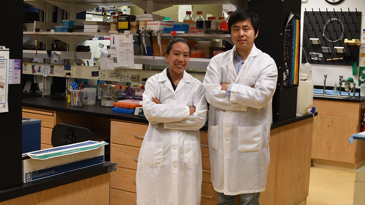 Two researchers in white lab coats stand in a lab
