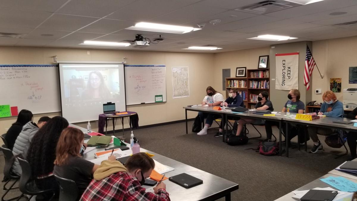 BJ Cummings is displayed on a large monitor at the front of a classroom full of high school students.